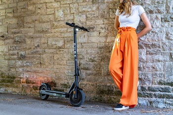 lady in orange trousers next to an e scooter with stone wall in backdrop 